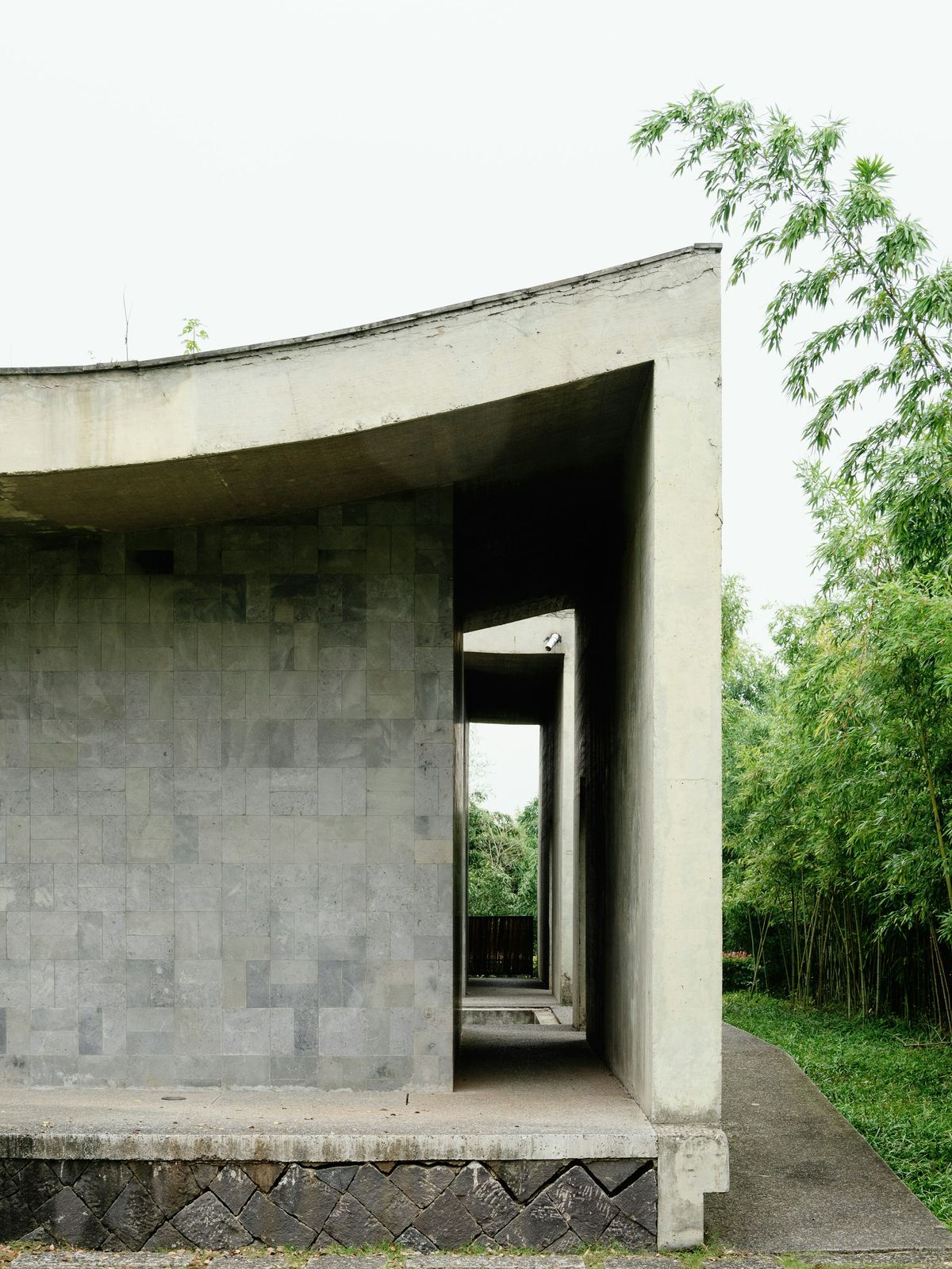 Curved concrete and stone building with a deep opening, among bamboo and trees