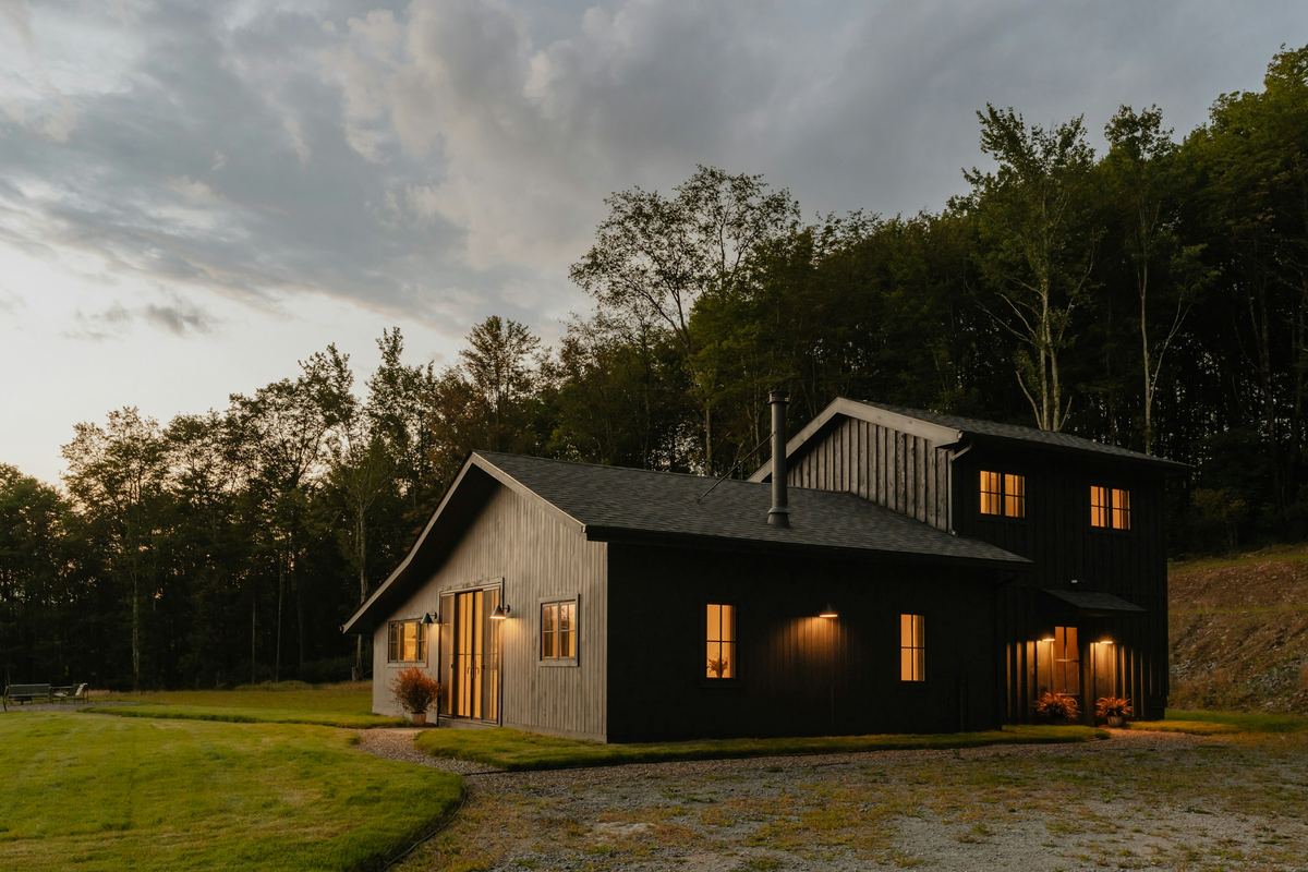 Timber-clad house with lit windows at dusk, framed by woodland